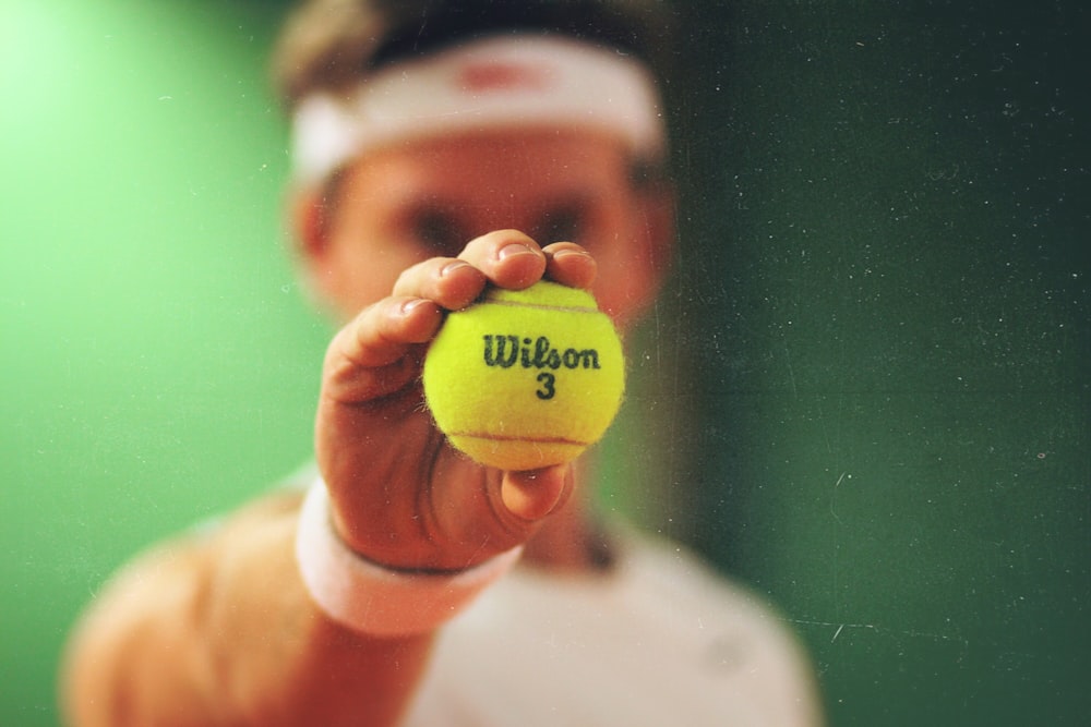 personne tenant une balle de tennis verte Wilson