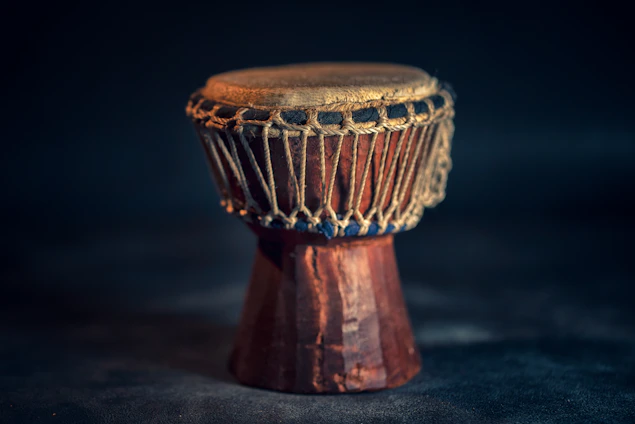 Close-up of a handcrafted mandar drum resting on textured red soil under soft natural light.