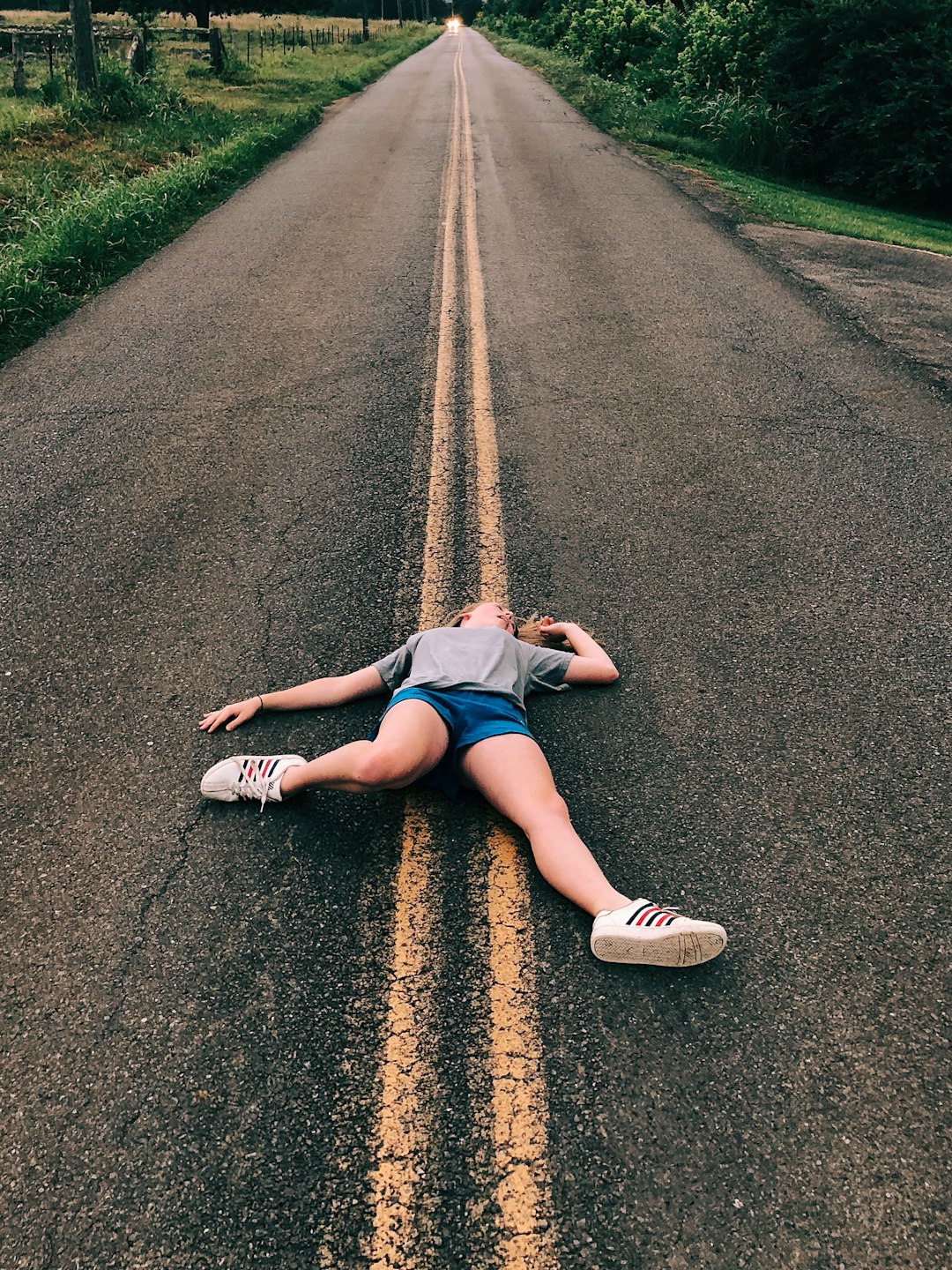 woman lying on gray concrete road near green field