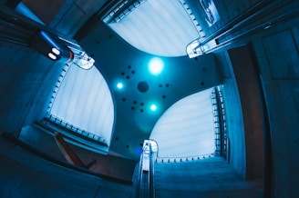 A futuristic architectural ceiling design with a central panel featuring numerous small circular lights and patterns. The surrounding walls are constructed from a sleek, modern material, and the lighting casts a cool blue hue over the entire structure.