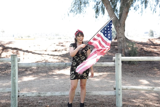 A proud woman wearing a patriotic First Ladies tee, standing in front of an American flag.