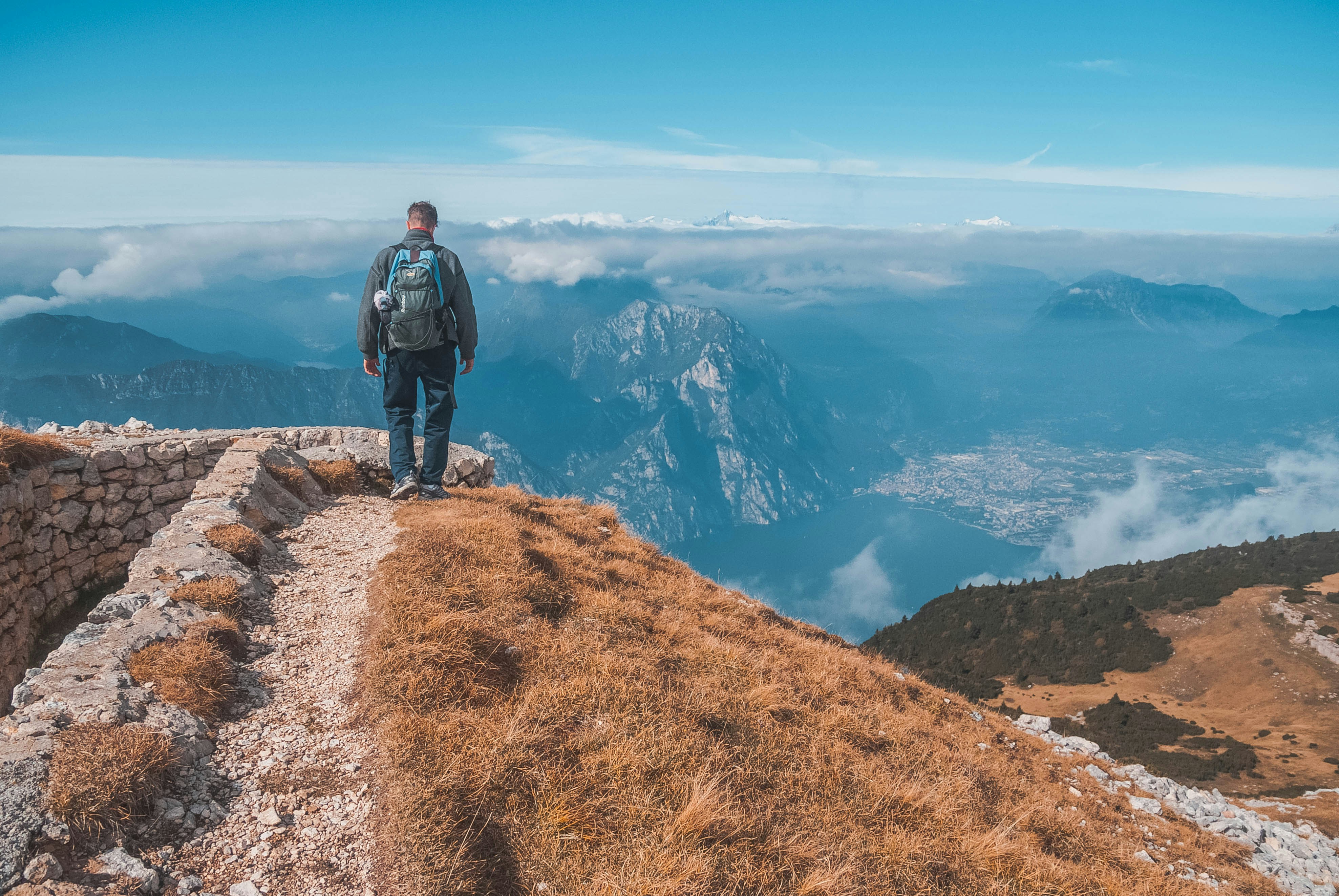 man carrying blue and grey backpack standing on brown hill under clear blue sky