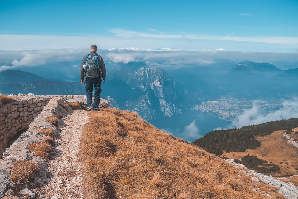 man carrying blue and grey backpack standing on brown hill under clear blue sky