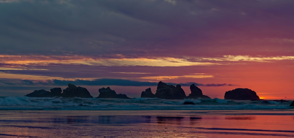 Silueta de rocas cerca de la orilla del mar bajo cielo naranja y gris