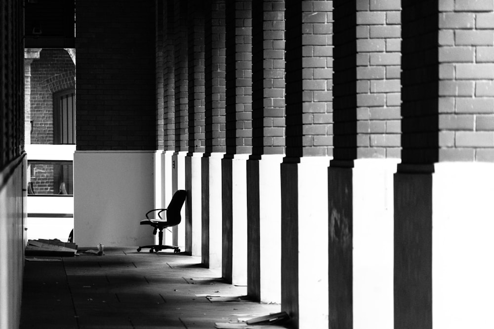 grayscale photography of black rolling chair on pathway with pillar post