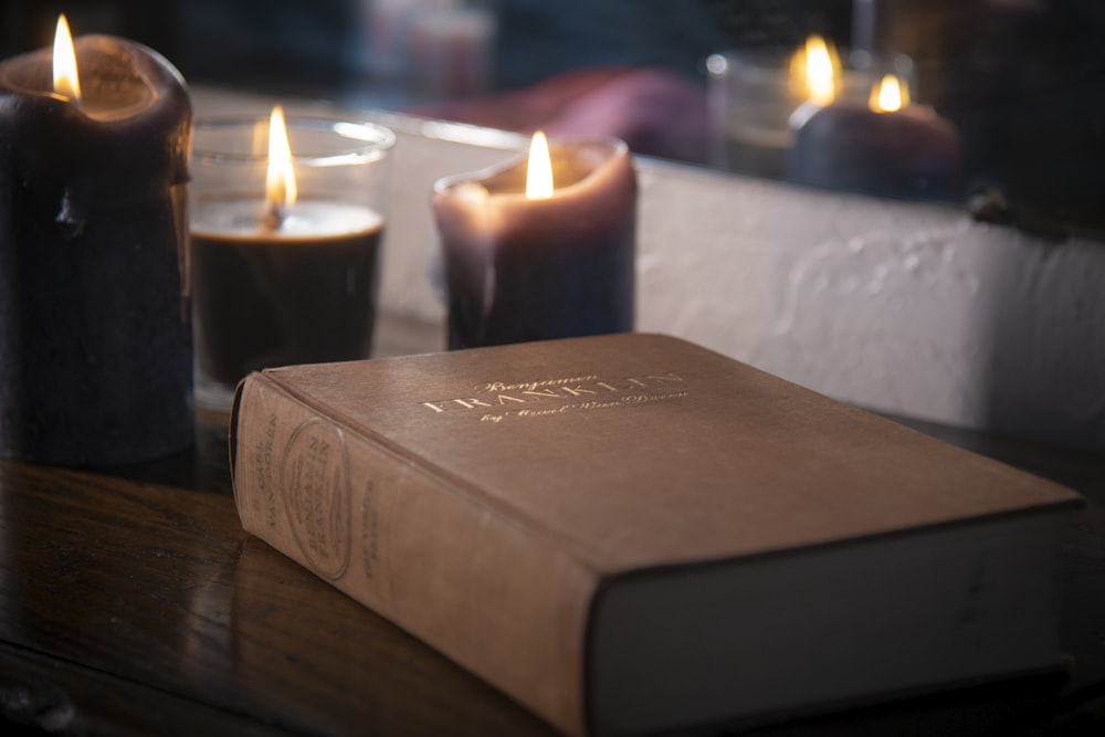 brown hardbound book near lighted pillar candles
