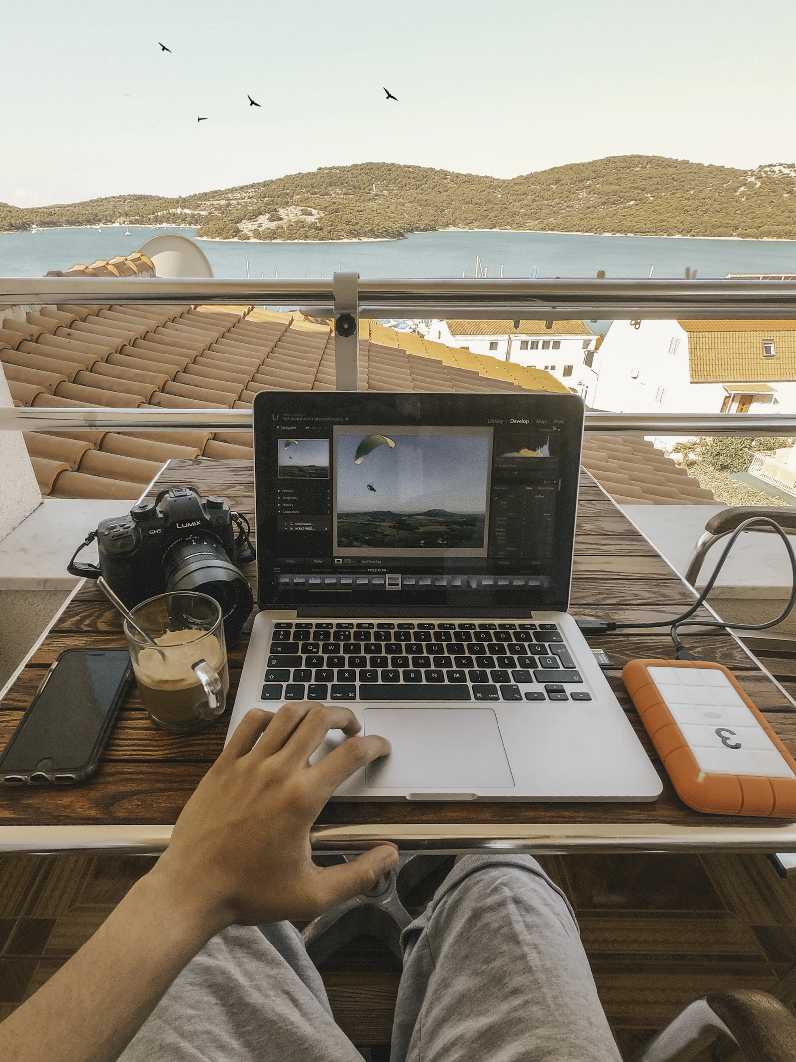 Person holding a MacBook Pro beside an orange portable power bank outdoors