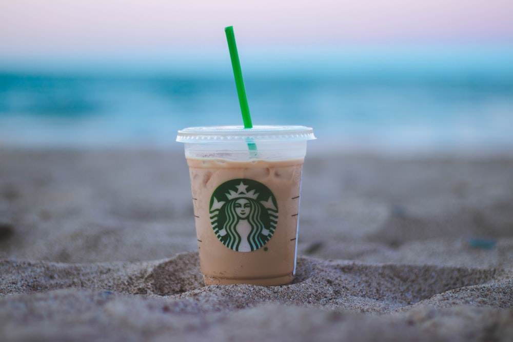 砂の上の透明なプラスチック製のスターバックスカップの浅い焦点の写真