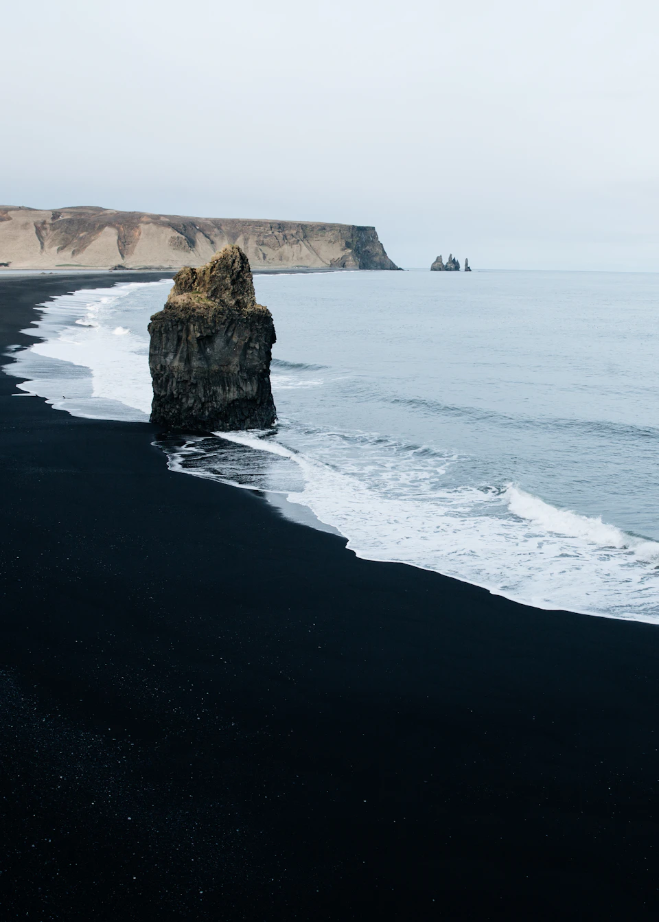 Large rock formation on a serene beach with dark blue ocean and sky nearby