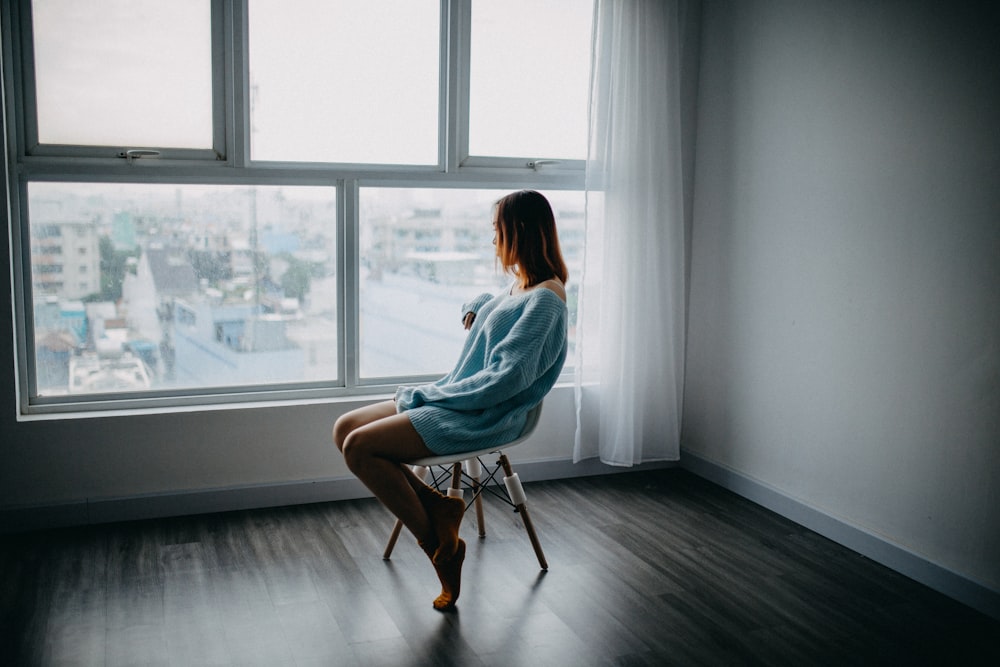 Mujer sentada en una silla marrón junto a la ventana de vidrio