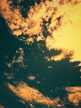 A celestial scene with scattered clouds illuminated by a warm light against a dark sky. Star-like specks are visible in the background, creating a sense of depth and serenity.