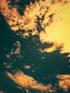 A celestial scene with scattered clouds illuminated by a warm light against a dark sky. Star-like specks are visible in the background, creating a sense of depth and serenity.
