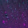 Water droplets cling to a surface, reflecting and refracting light that creates a mix of neon colors, predominantly purple and teal. The droplets vary in size and are scattered across the surface, creating a visually striking effect.