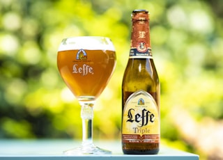 selective focus photo of Leffe triple glass bottle beside filled wine glass at daytime