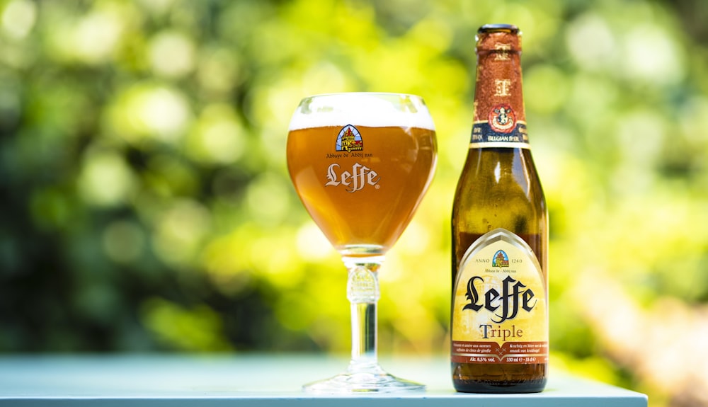 selective focus photo of Leffe triple glass bottle beside filled wine glass at daytime