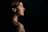 Profile of a professional woman with short hair, illuminated softly against a deep charcoal backdrop with gold accents.
