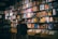 A record store with a wall lined with colorful vinyl albums, featuring various cover art designs and portraits. Two people stand in front of a wooden crate filled with more records, browsing the collection.