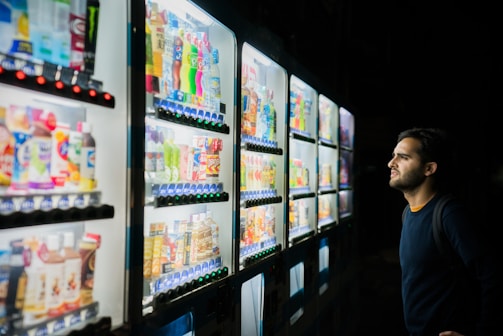 Close-up of a hand selecting an energy drink from a Snaxi vending machine.