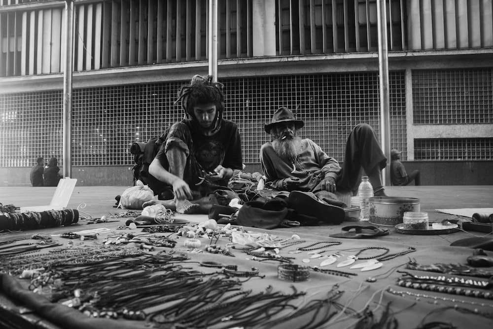 grayscale photo of two man sitting on the ground