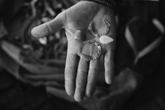 A close-up of an outstretched hand holding various small metallic and bead-like objects. The background is softly blurred, drawing focus to the detailed textures of the hand and the items.