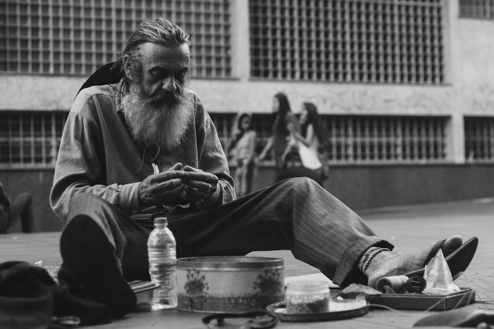 grayscale photo of man sitting on ground with bottle