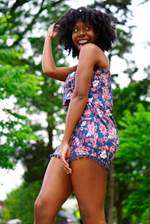 A joyful woman with curvy silhouette wearing a vibrant floral dress, smiling confidently outdoors.