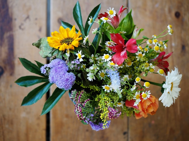 A colorful bouquet featuring sunflowers, lilies, and daisies on a rustic wooden table