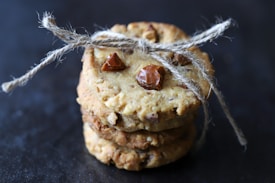 Three stacked cookies tied together with rustic twine, featuring visible chunks of nuts and chocolate on a dark background.
