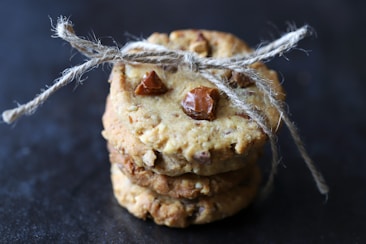 Three stacked cookies tied together with rustic twine, featuring visible chunks of nuts and chocolate on a dark background.