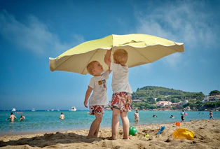 two children playing under umbrella on seashore