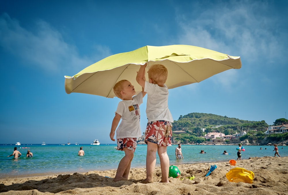 zwei Kinder spielen unter Sonnenschirm am Meer