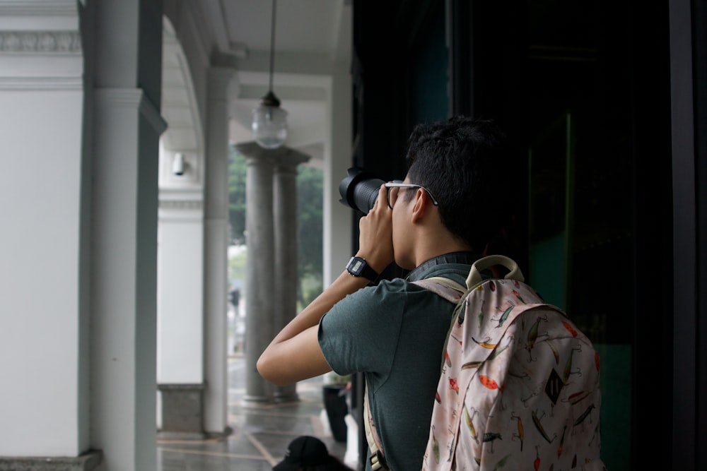 man carrying backpack while using DSLR camera