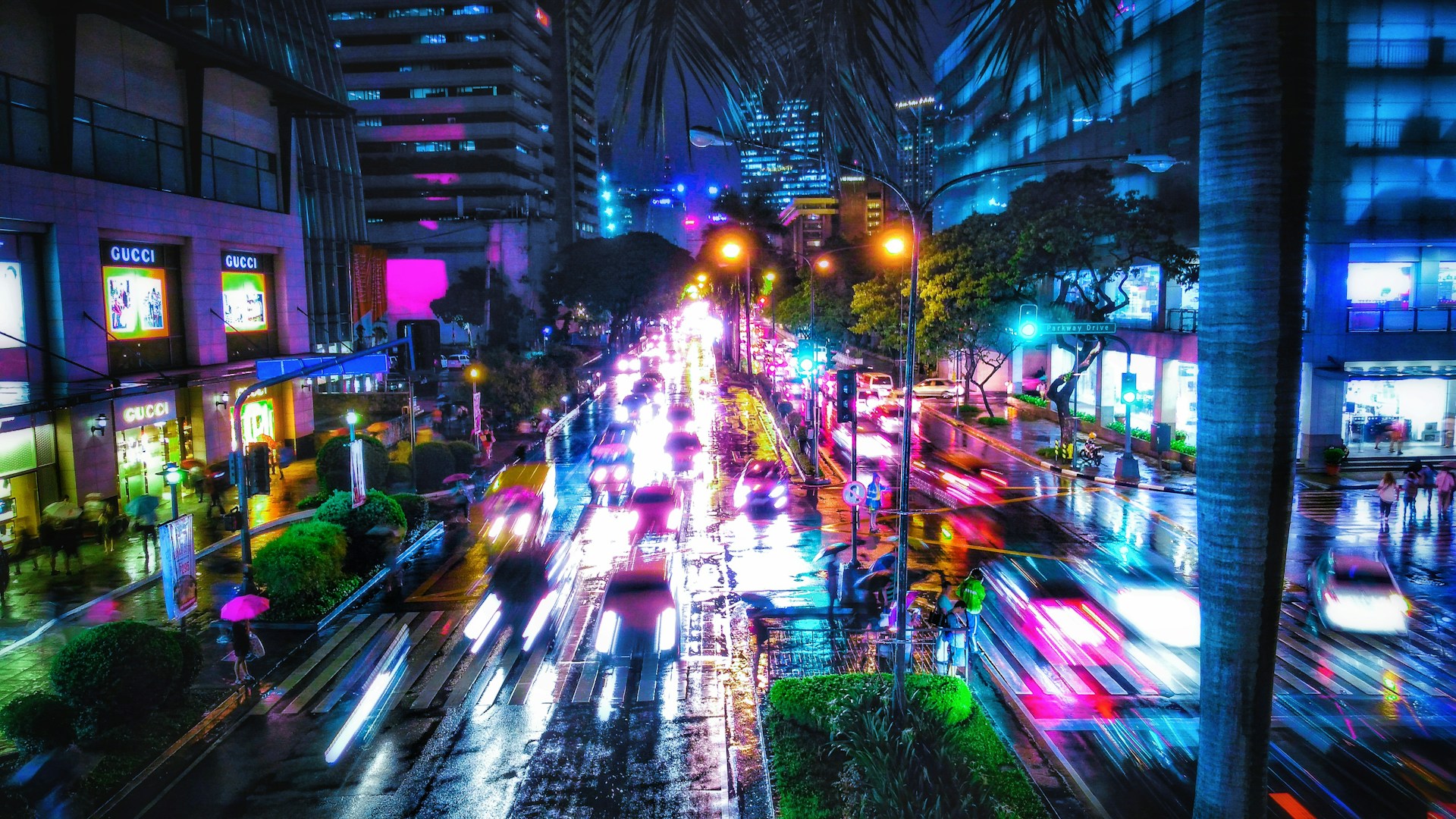 A bustling city street at dusk, with colorful lights reflecting off wet pavement and blurred motion of people walking.