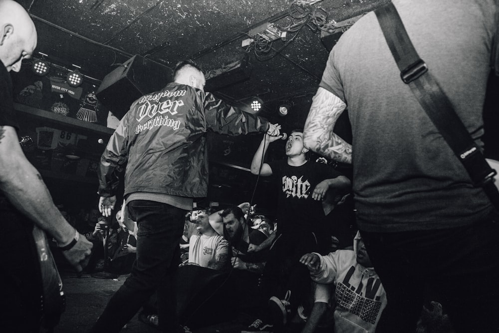 grayscale photo of man holding microphone and surrounded by people