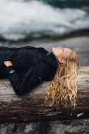 woman in black zip-up jacket leaning on large log at daytime