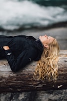 woman in black zip-up jacket leaning on large log at daytime