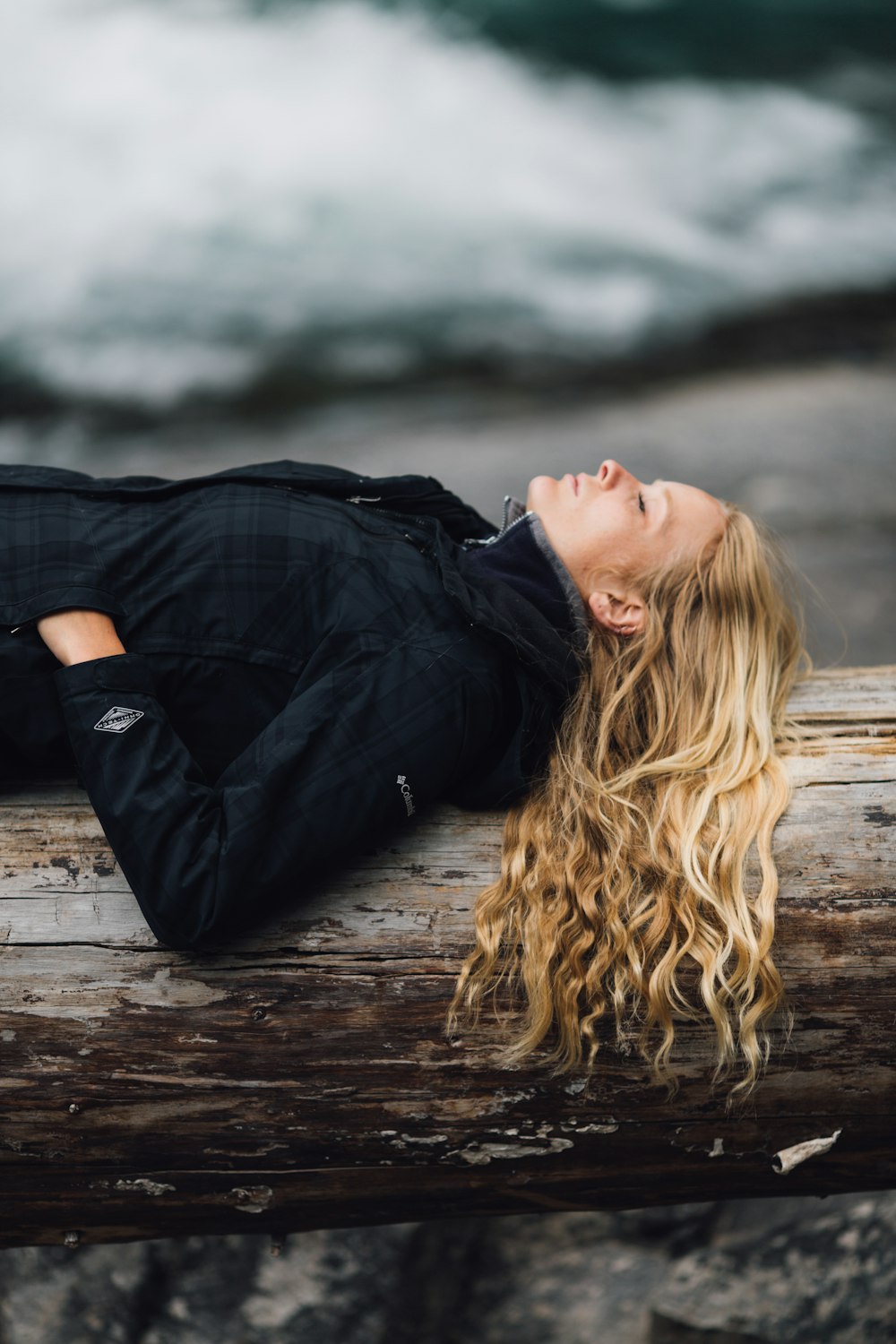 woman in black zip-up jacket leaning on large log at daytime