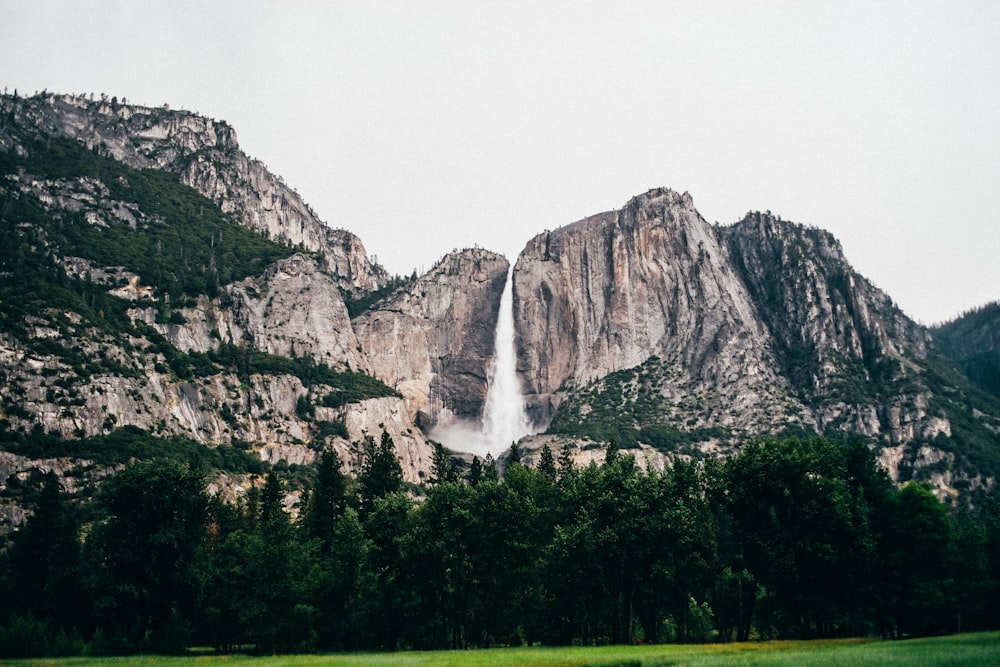 rocky mountain across green grass field under white sky