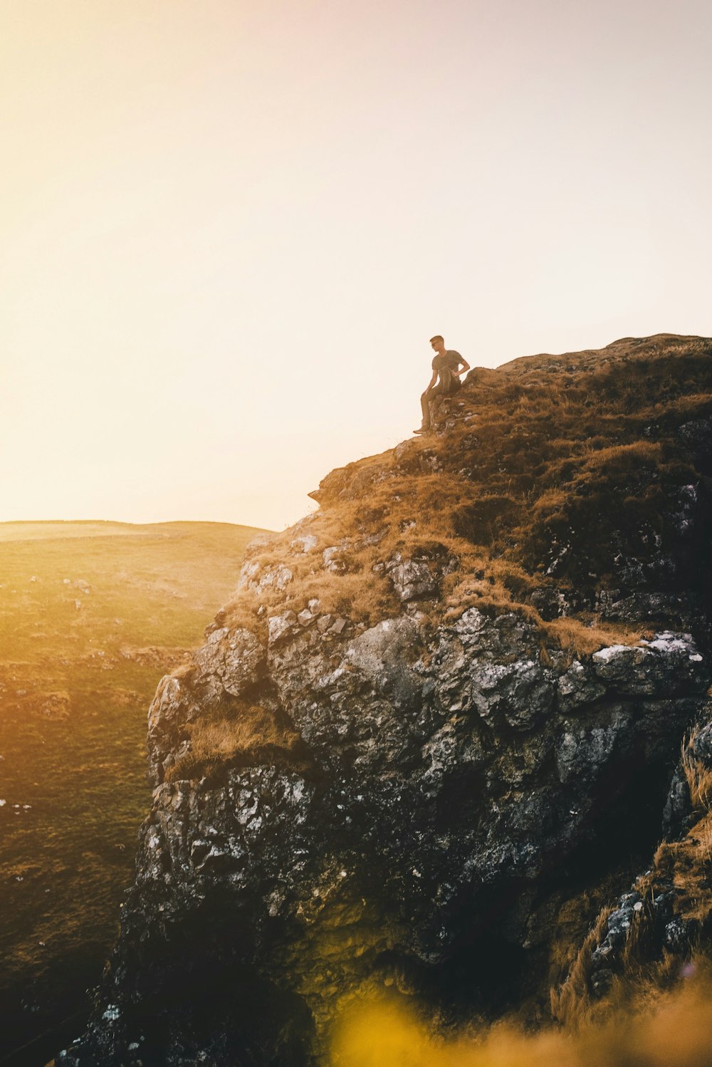 man sitting on cliff during golden hour