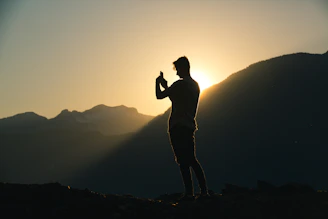 Close-up of a hiker’s hand tracing a detailed map on a smartphone, with the sun setting over Mijas mountains in the background.