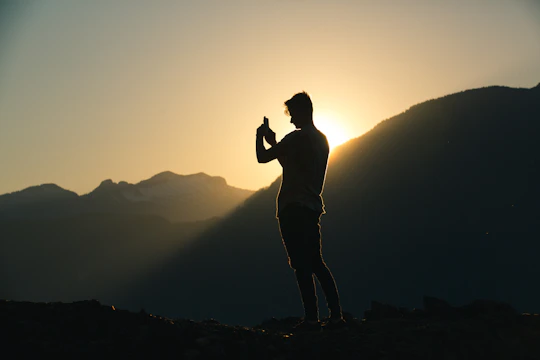 Close-up of a hiker’s hand tracing a detailed map on a smartphone, with the sun setting over Mijas mountains in the background.