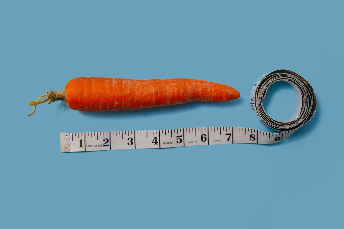 A 7.25 inch carrot against a sky blue background.  Underneath is a cloth measure tape uncoiled to the 8" mark.