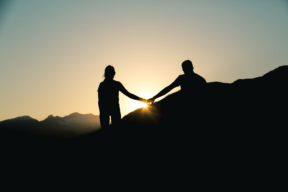 silhouette of man and woman holding hands while walking under gray sky during daytime