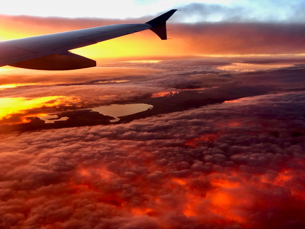 Clouds stretch to the horizon bathed in golden hour light, viewed from above with warm orange and pink hues filling the sky.. Photo by Alex Jekowsky on Unsplash.
