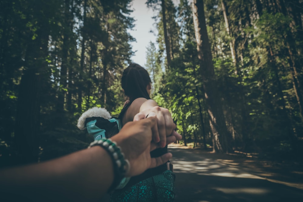 woman holding hand of a person while walking on road between trees