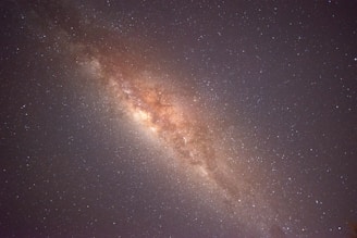 A vast expanse of stars is visible, forming a dense, cloudy band across the image. The central region is brighter and filled with more concentrated stardust and celestial bodies, characteristic of a galaxy. Surrounding this area is a multitude of smaller stars scattered across a dark, night sky.