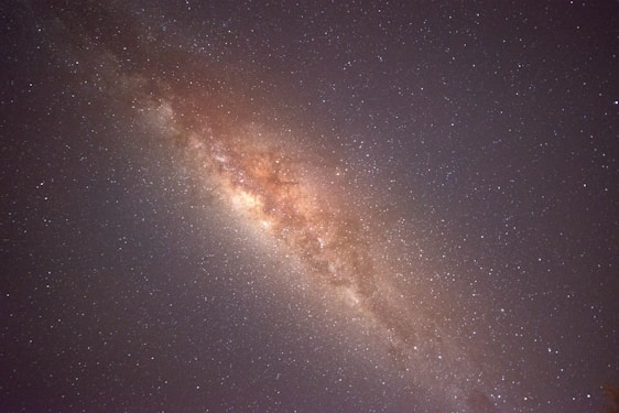 A vast expanse of stars is visible, forming a dense, cloudy band across the image. The central region is brighter and filled with more concentrated stardust and celestial bodies, characteristic of a galaxy. Surrounding this area is a multitude of smaller stars scattered across a dark, night sky.