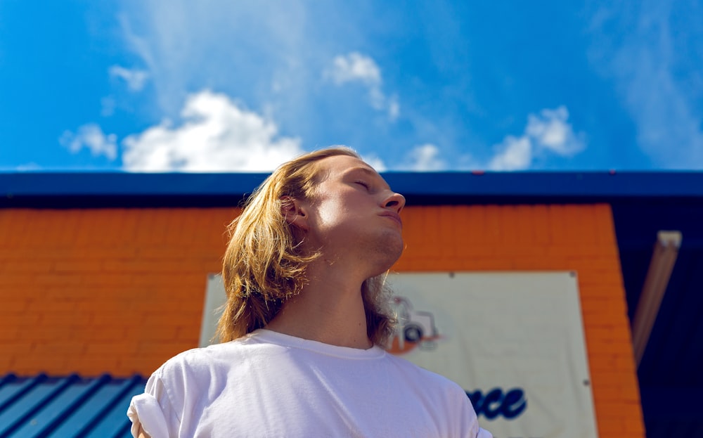 man wearing white crew-neck t-shirt while standing near building