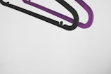 Two plastic hangers, one black and one purple, are suspended against a plain white background. They are overlapping slightly, with a minimalist and modern aesthetic.