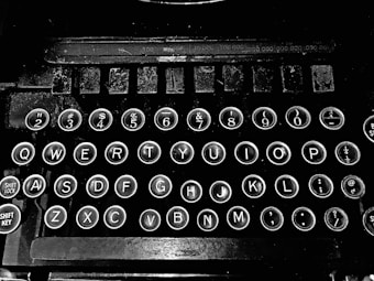 The image displays a vintage typewriter keyboard with round keys featuring letters, numbers, and symbols. The keys are well-spaced and surrounded by a metallic rim, set against a black background, highlighting their classic design.